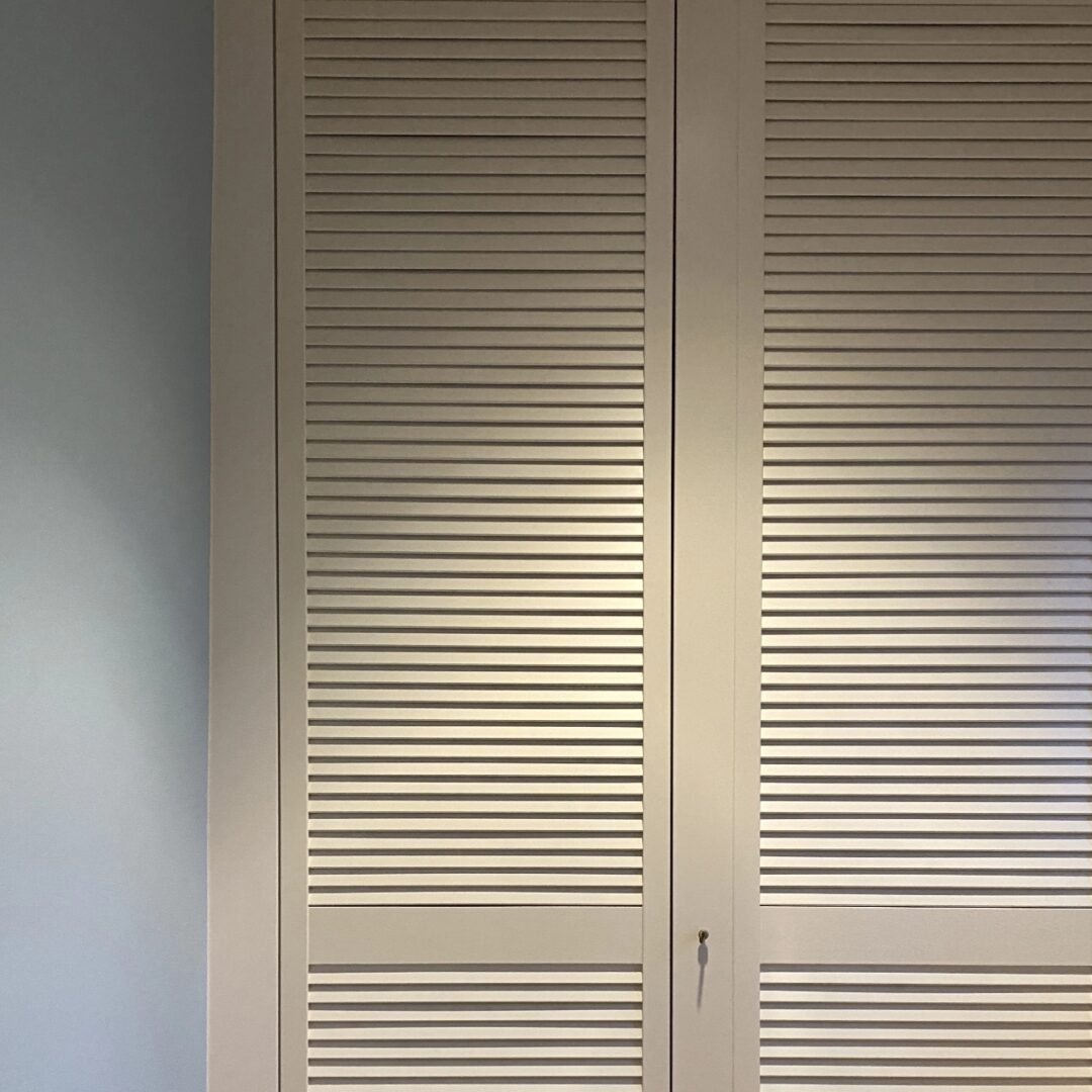 Garderobenschrank mit großen abschließbaren Türen im Lamellen-Look neben einer hellblauen Wand
