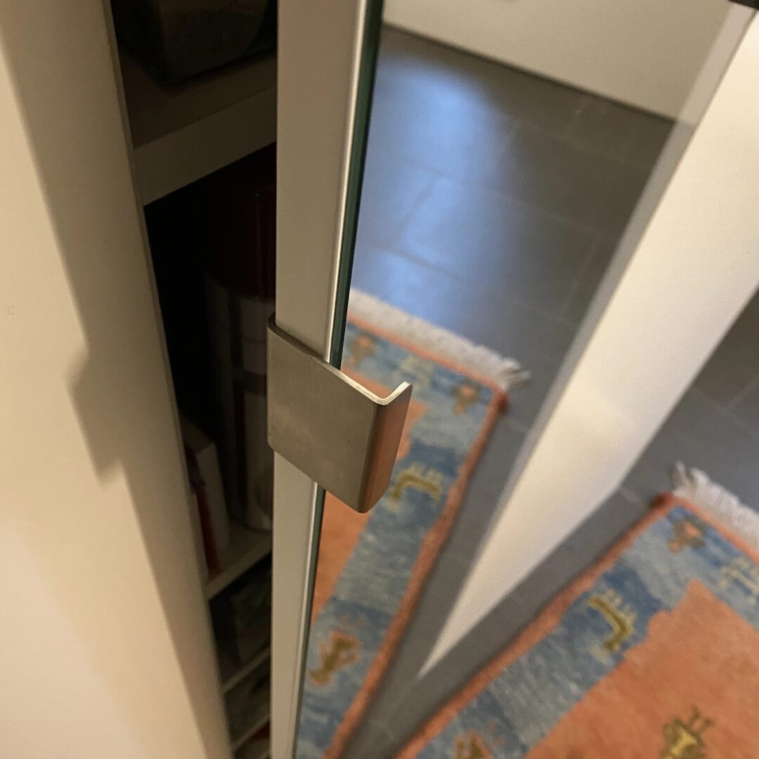 Leicht geöffnete Spiegeltür eines weißen Garderobenschranks mit einem simplen Metallgriff
