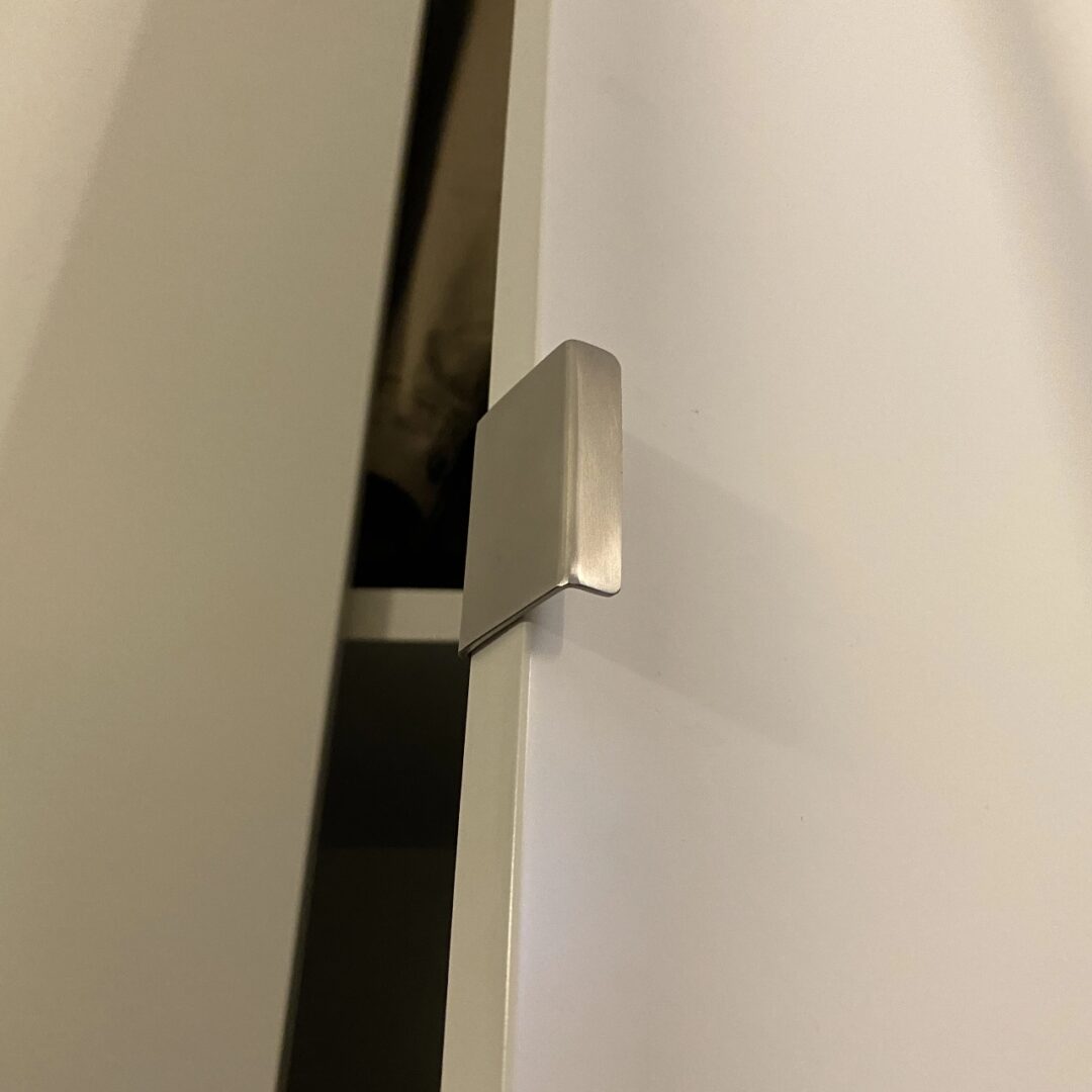 Nahaufnahme einer leicht geöffneten Tür eines weißen Schrankes mit einem eckigen Metallgriff