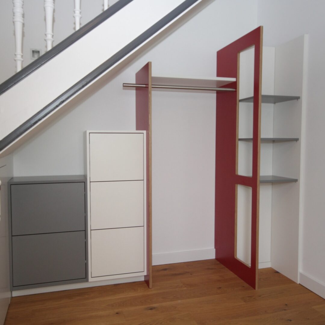 Maßgefertigte Garderobenmöbel mit verschiedenen Elementen in den Farben grau, weiß und rot unter einer Treppe
