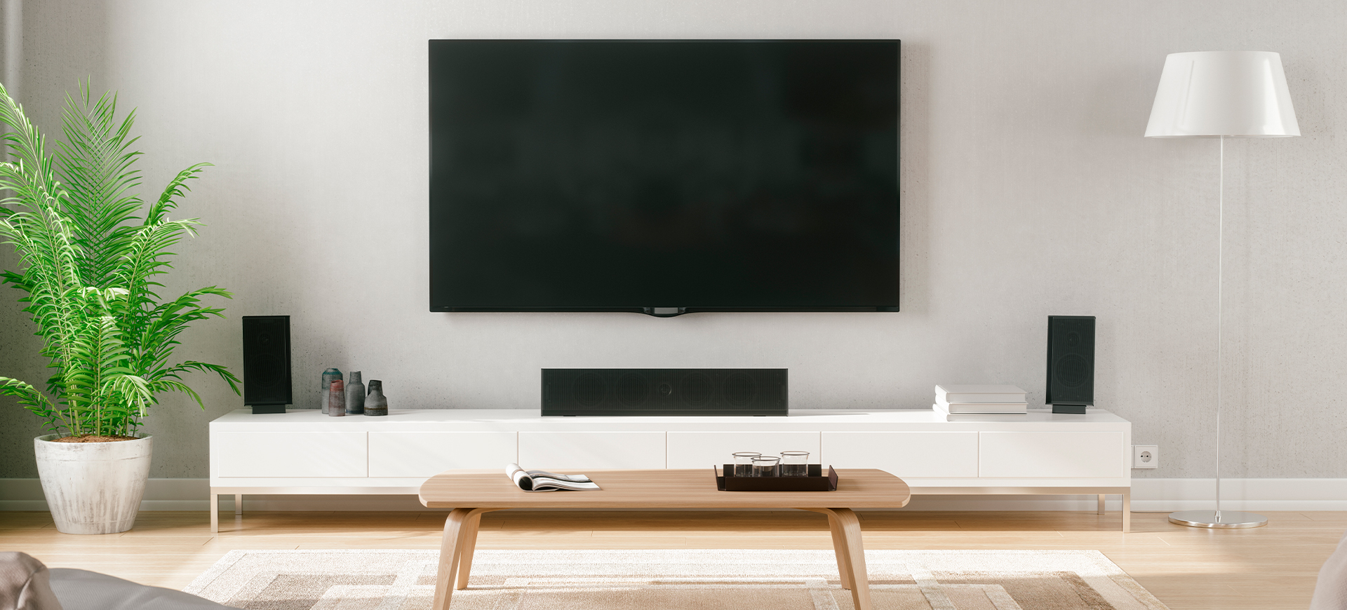 Sicht vom Sofa auf einen an der Wand hängenden Fernseher und einem Soundsystem auf einem geschlossenen, weißen Hifi-Lowboard