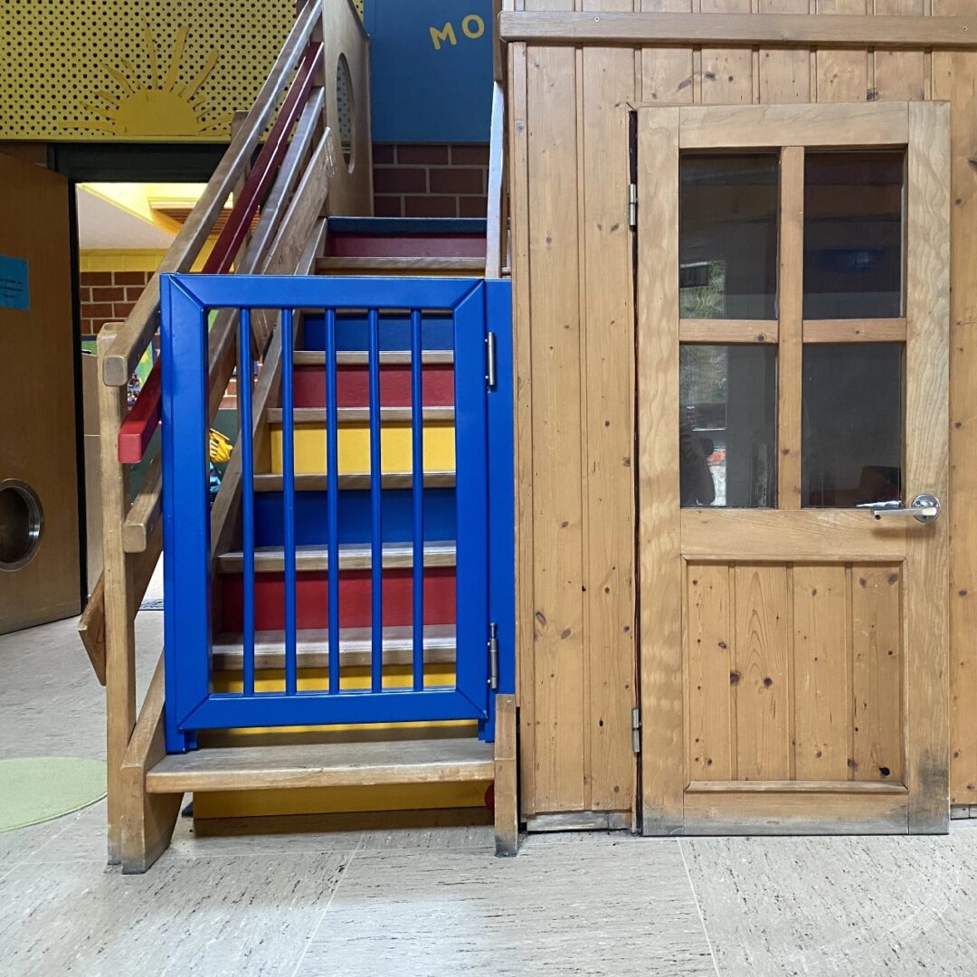 Blaues Treppenschutzgitter an der bunt lackierten Außentreppe eines Spielhauses in einem Kindergarten