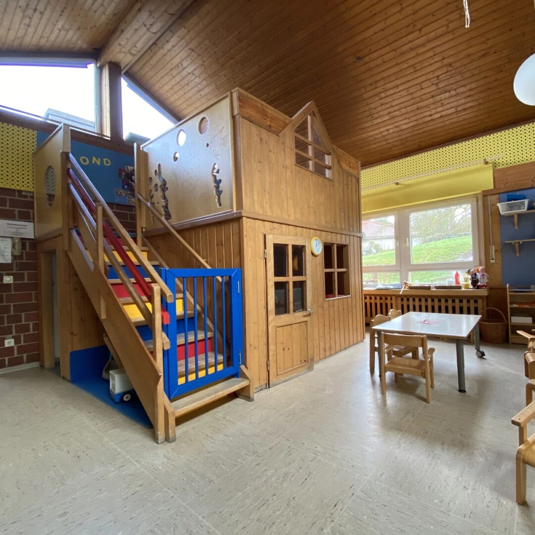Großes maßgefertigtes zweistöckiges Spielhaus mit außenliegender bunter Treppe in einem großen Kindergartenraum