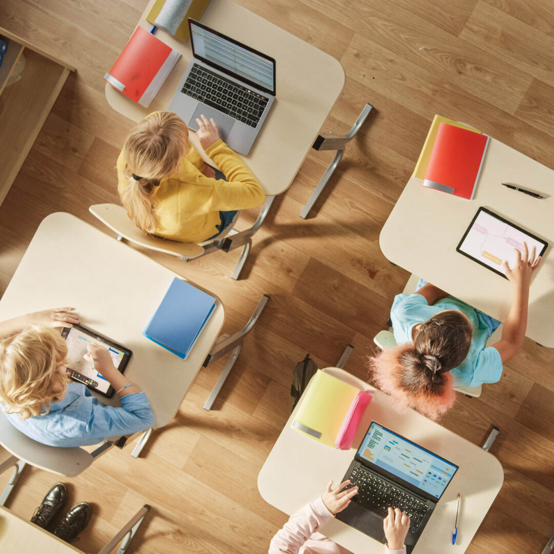 Vogelperspektive auf 4 Kinder, die an maßgefertigten Schulmöbeln mit ihren digitalen Endgeräten lernen