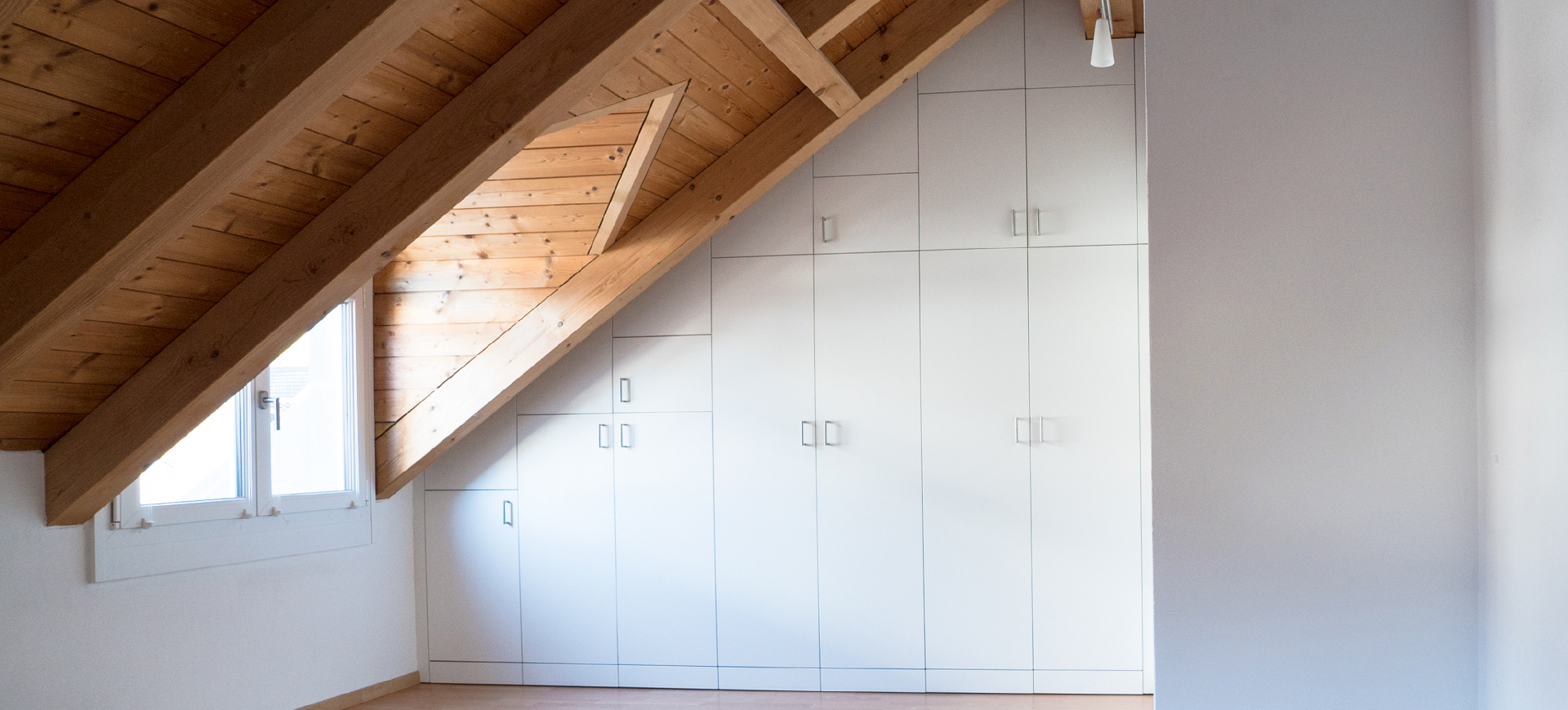 Weißer, schlichter Dachschrägen-Schrank mit zahllosen Türen bietet versteckten Stauraum