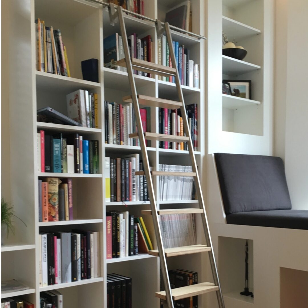 Weißes Bücherregal aus Holz mit verschieden großen Fächern und einer integrierten gepolsterten Sitzfläche