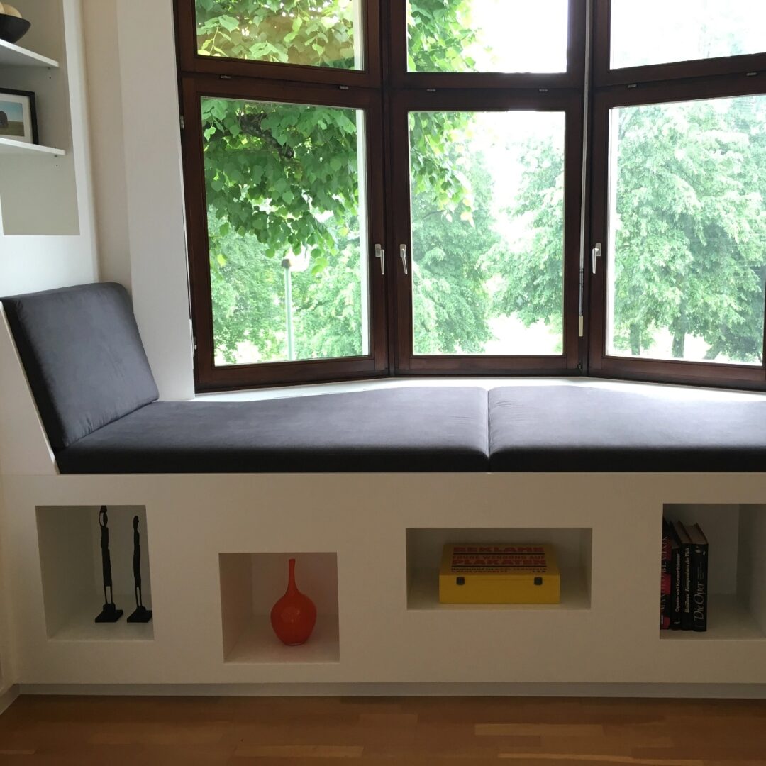 Maßgefertigte gepolsterte Sitzbank unter einem Erker-Fenster mit integrierten Ablagefächern für Bücher und Deko