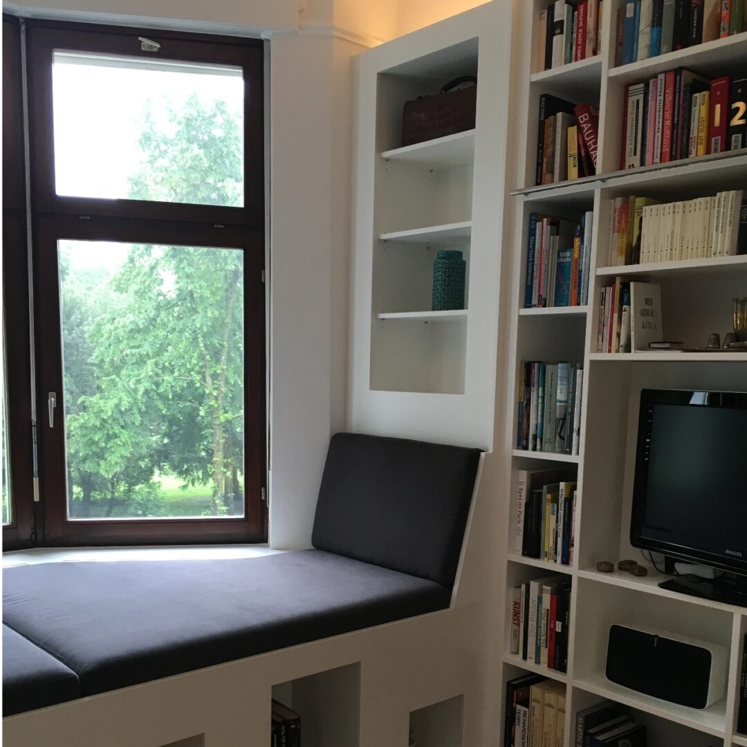 Sitz-Liegefläche unter einem Erker-Fenster mit anschließendem Bücherregal aus weiß lackiertem Massivholz