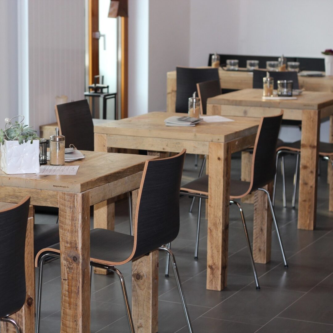 Freundlicher Essbereich eines Restaurants mit quadratischen Holztischen mit jeweils zwei schwarzen Stühlen mit Metallbeinen