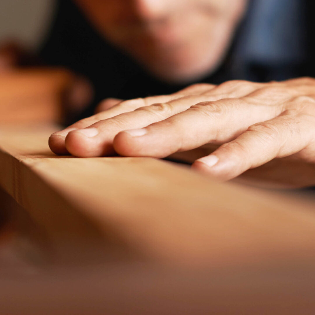 Nahaufnahme der Hand eines Schreiners, die über ein Stück Holz streicht