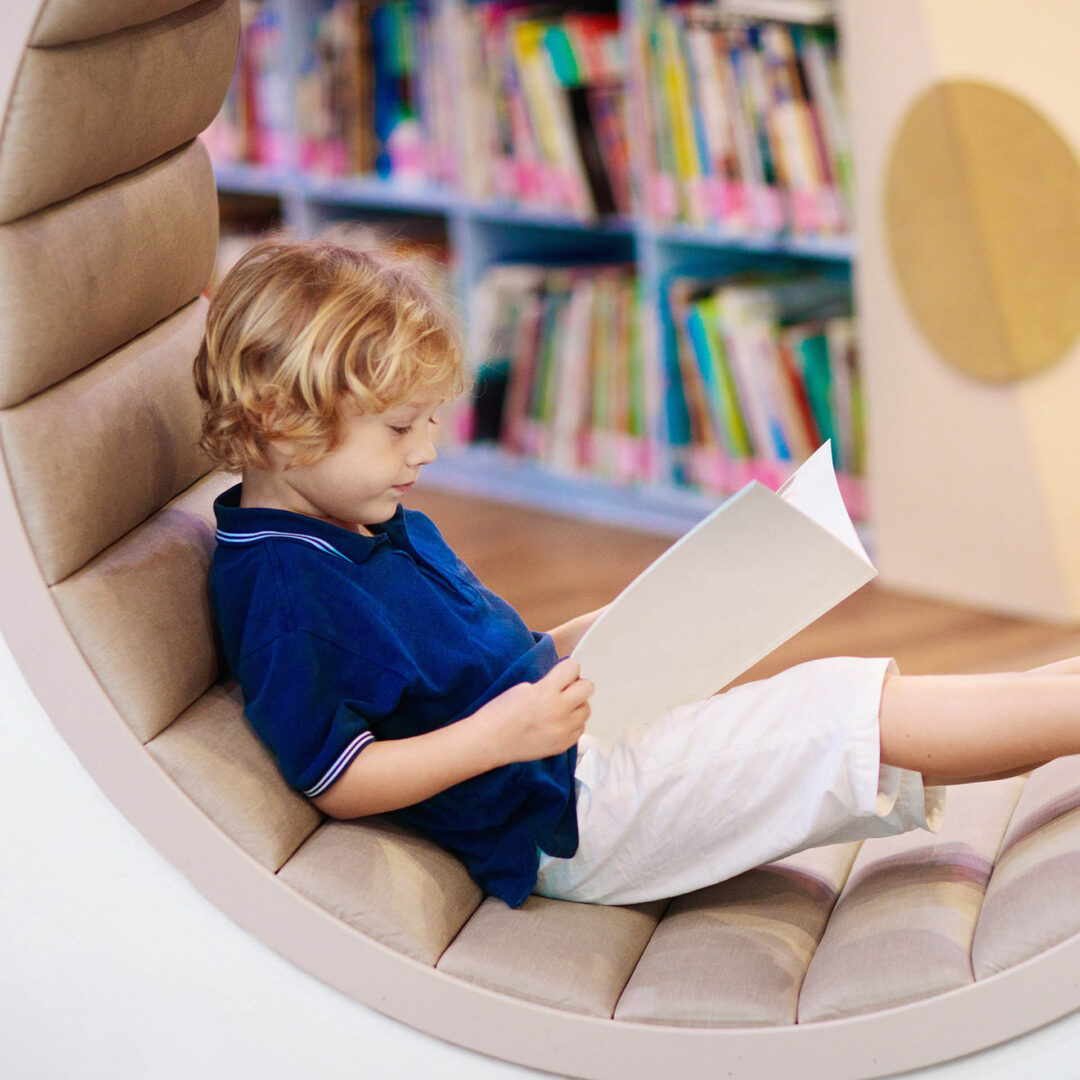 Lesendes Kind in einer ergonomisch geformten Sitzbank mit beigem Polsterbezug in einer OGS