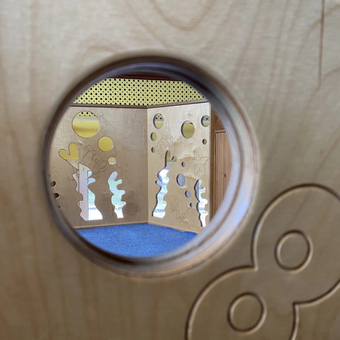 Blick durch ein rundes Loch in einer Spielwand auf eine weitere Spielwand mit Meer-Motiven