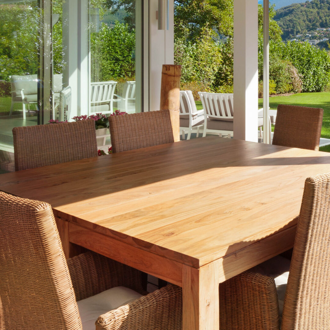 Großer schlichter Gartentisch aus Massivholz für acht Personen mit Rattenstühlen auf einer sonnigen Terrasse