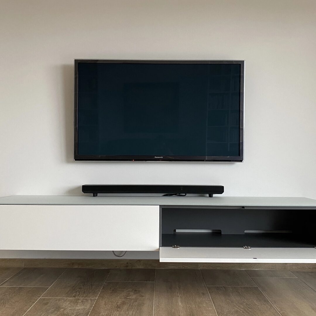 Weißes TV-Möbel mit einer geöffneten und einer geschlossenen Schranktür unter einem hängenden Fernseher