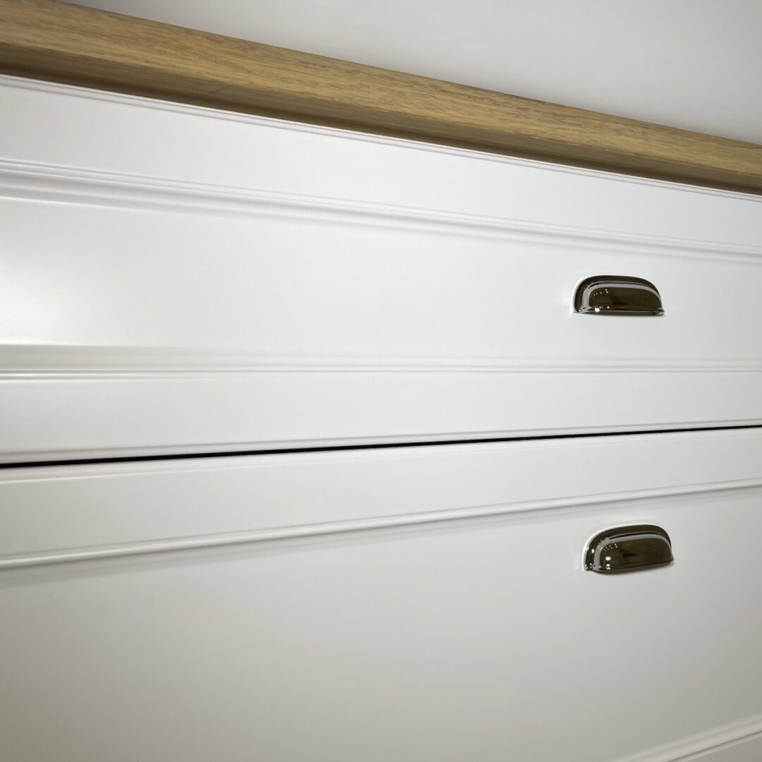 Nahaufnahme eines weißen Waschtischunterschranks im Landhausstil mit eleganten Einkerbungen und Metallgriffen