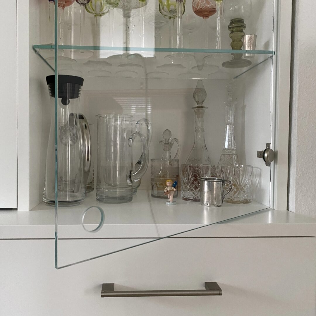 Nahaufnahme eines weißen Holzkorpus mit Glastür und Glaseinlegeböden zur Präsentation diverser Gläser