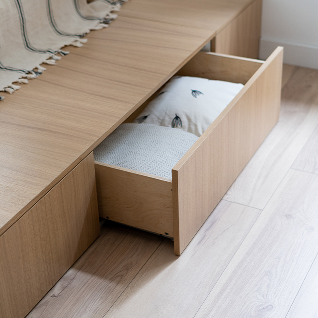 Bett aus hellem Massivholz mit integrierten, grifflosen Schubladen für versteckten Stauraum im Schlafzimmer