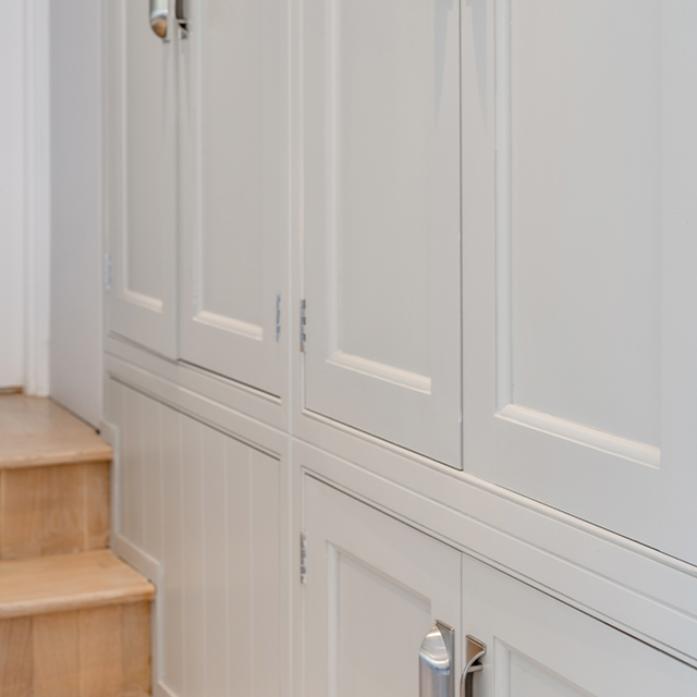 Ein an die Treppe angepasster Garderobenschrank mit weißen Türen im klassischen Landhaus-Stil