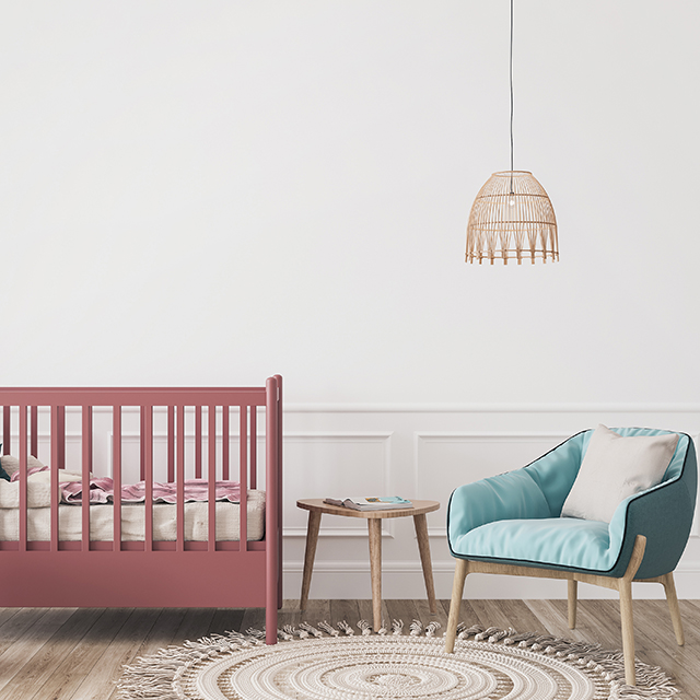 Altrosa Baby-Gitterbett neben einem hellblauen Stillsessel in einem Kinderzimmer mit weißen Wänden