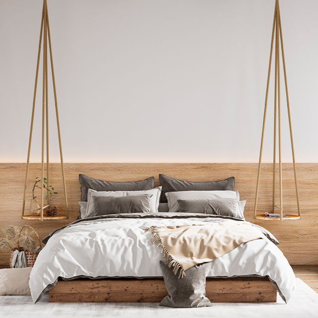 Ein Massivholzbett für zwei Personen vor einer mit Holz verkleideten Wand in einem hellen Schlafzimmer