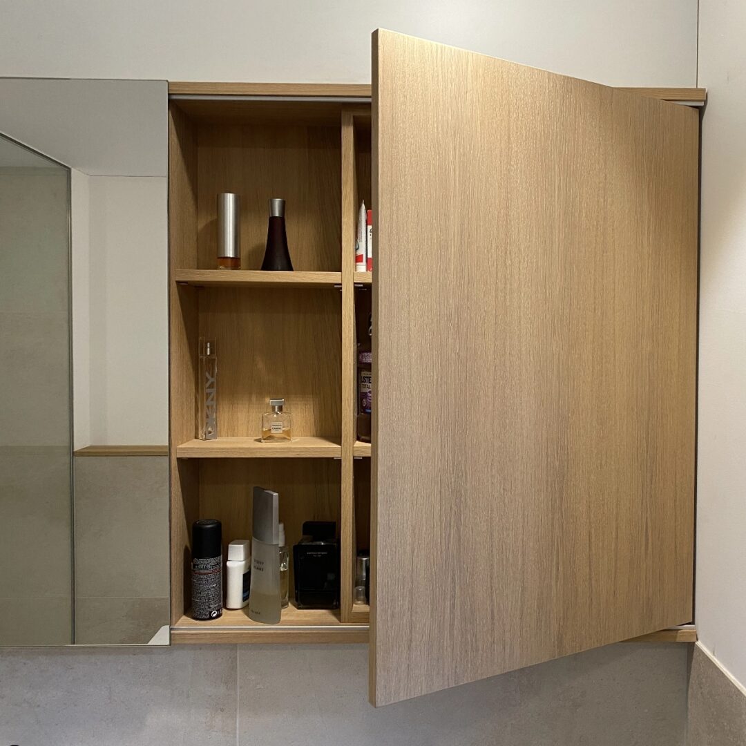 Hängender Badschrank mit Spiegeltür, offenen Fächern und einer Schranktür im schlichten Holzlook
