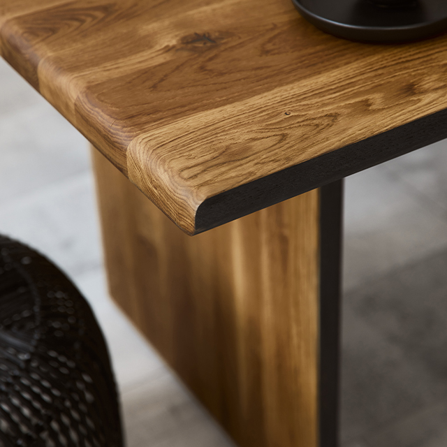 Nahaufnahme eines Esstischs aus dunklem Massivholz mit abgerundeter Tischkante und einem durchgehenden Tischbein