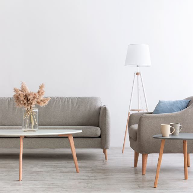 Hellgraue Sitzgruppe mit zwei skandinavischen Couchtischen aus hellen Holzbeinen und ovalen Tischplatten