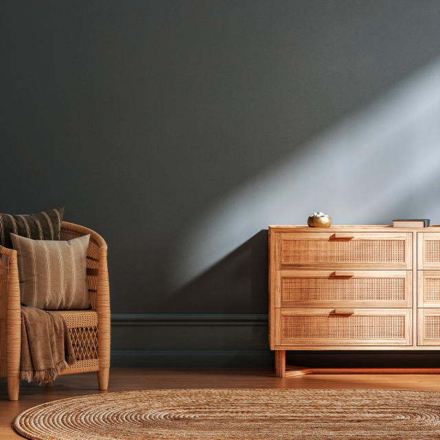 Kommode aus hellem Holz mit Schubladen im ausgefallenen Rattan-Look vor einer dunkelgrauen Wand als Hingucker