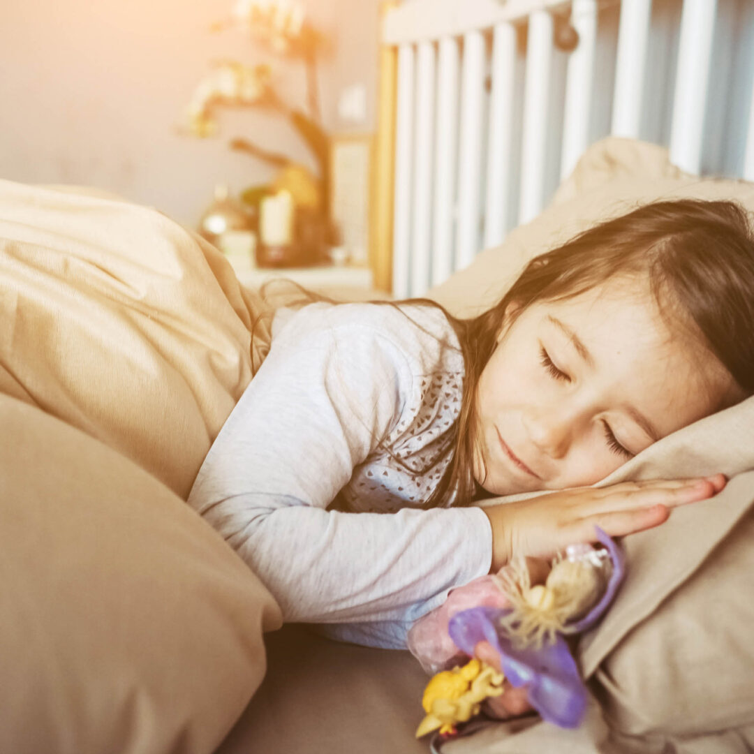 Schlafendes Kind in einer beigen Bettwäsche mit Spielzeug in der Hand
