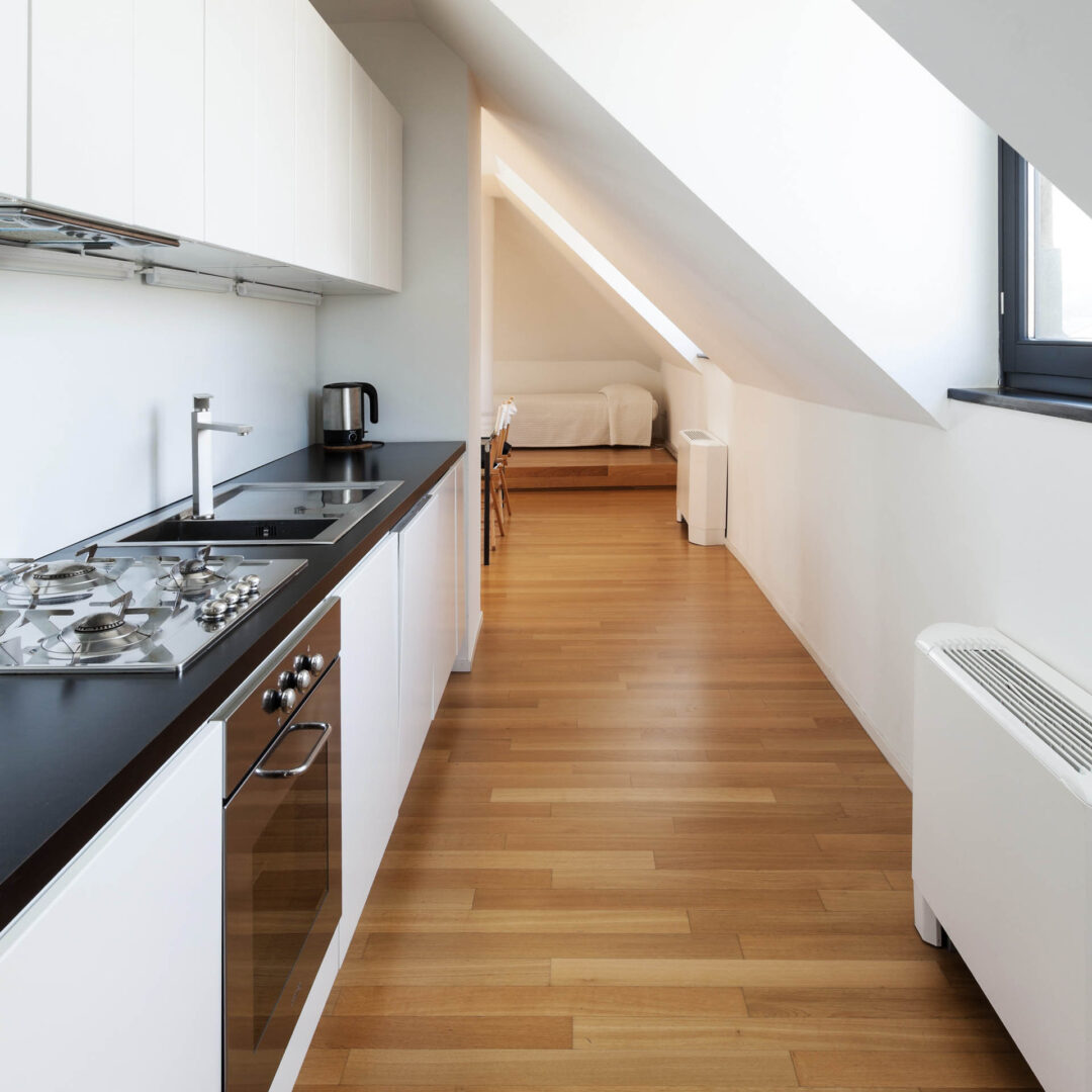 Maßgefertigte weiß-graue Küchenzeile in einem schmalen Raum mit starker Dachschräge